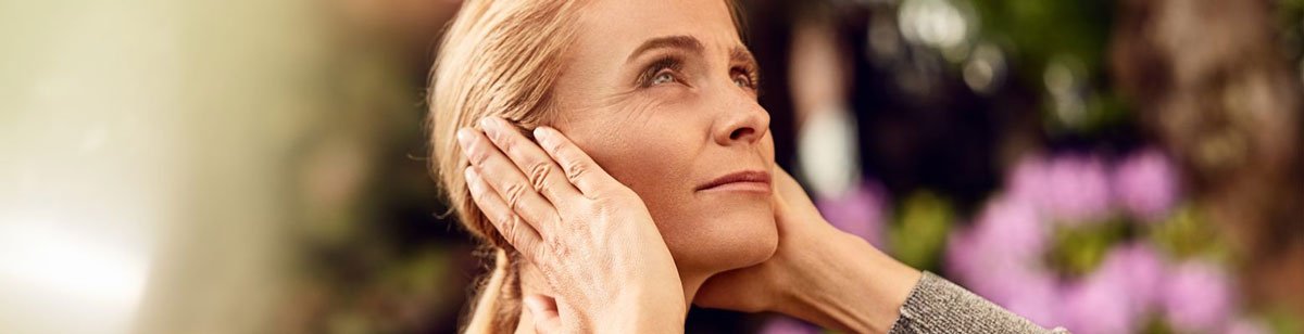 Woman standing outside covering her ears with both of her hands